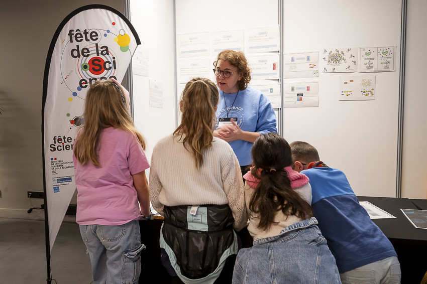 Zoom sur des jeunes au festival des sciences écoutant l'explication d'une dame
